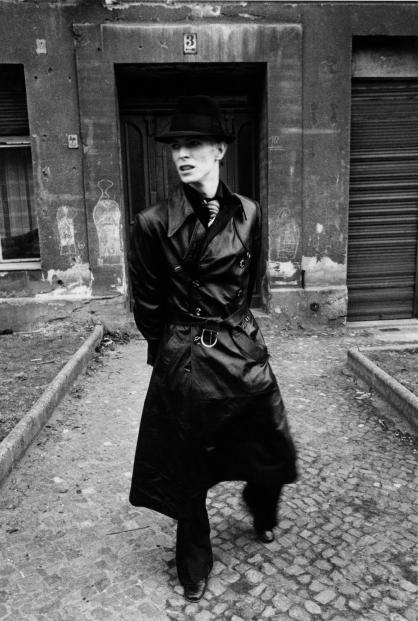 David Bowie dressed in a full length black leather trench coat and hat in East Berlin, 1976