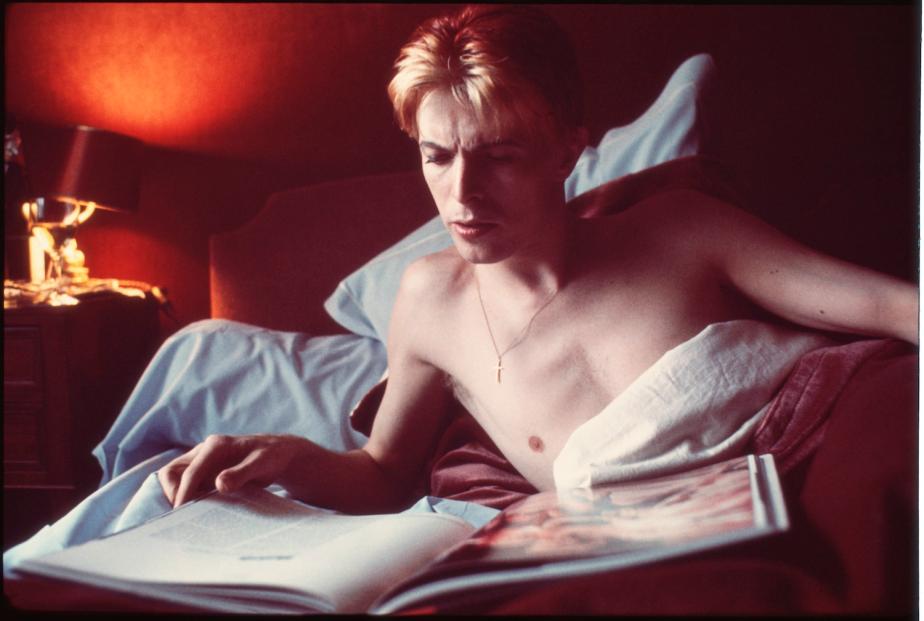 David reads through a book in his bed during a rare quiet morn- ing in his suite at L’Hotel in Paris, 1976